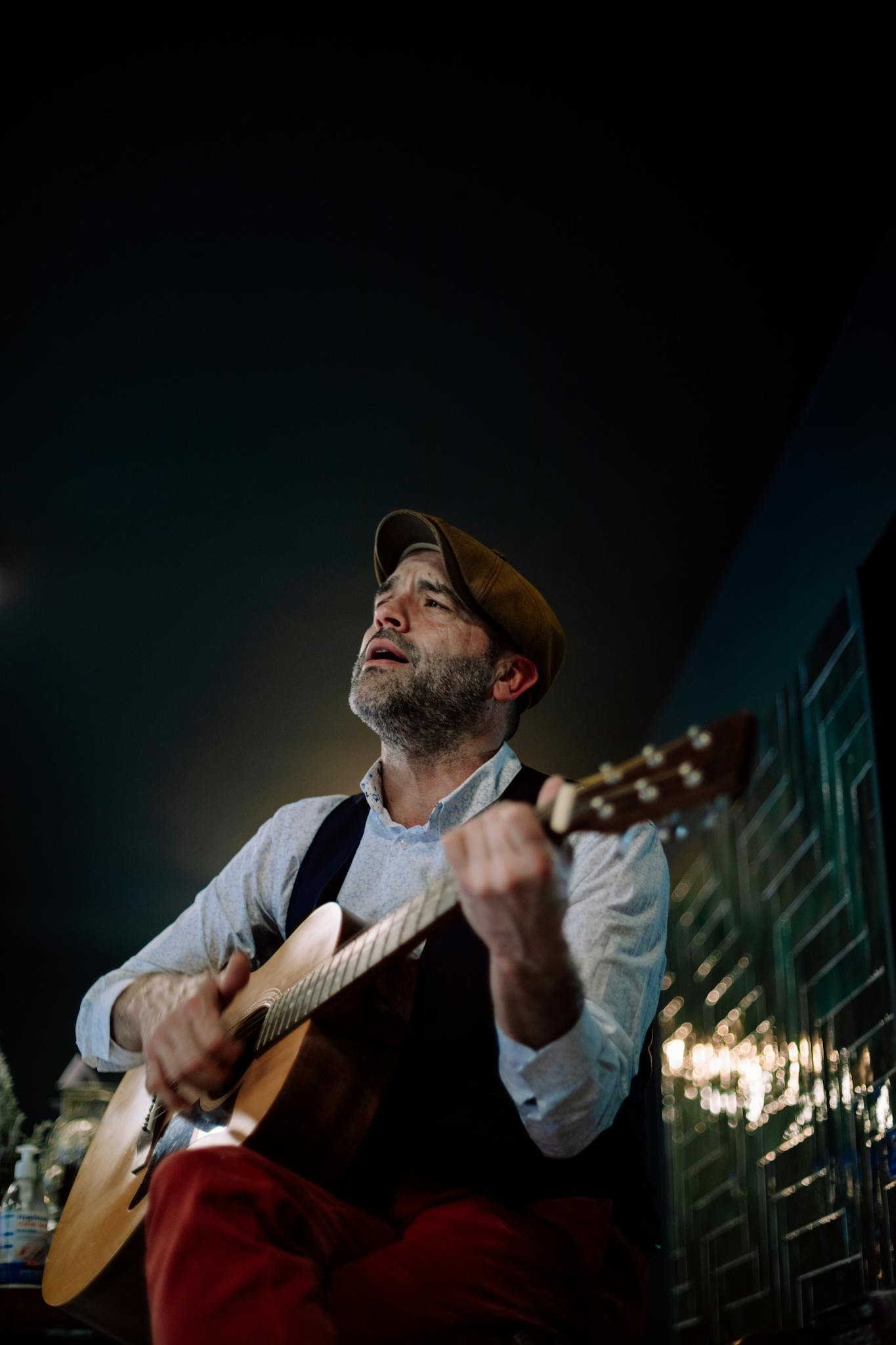 A bearded man passionately singing and playing guitar indoors in Geneva.