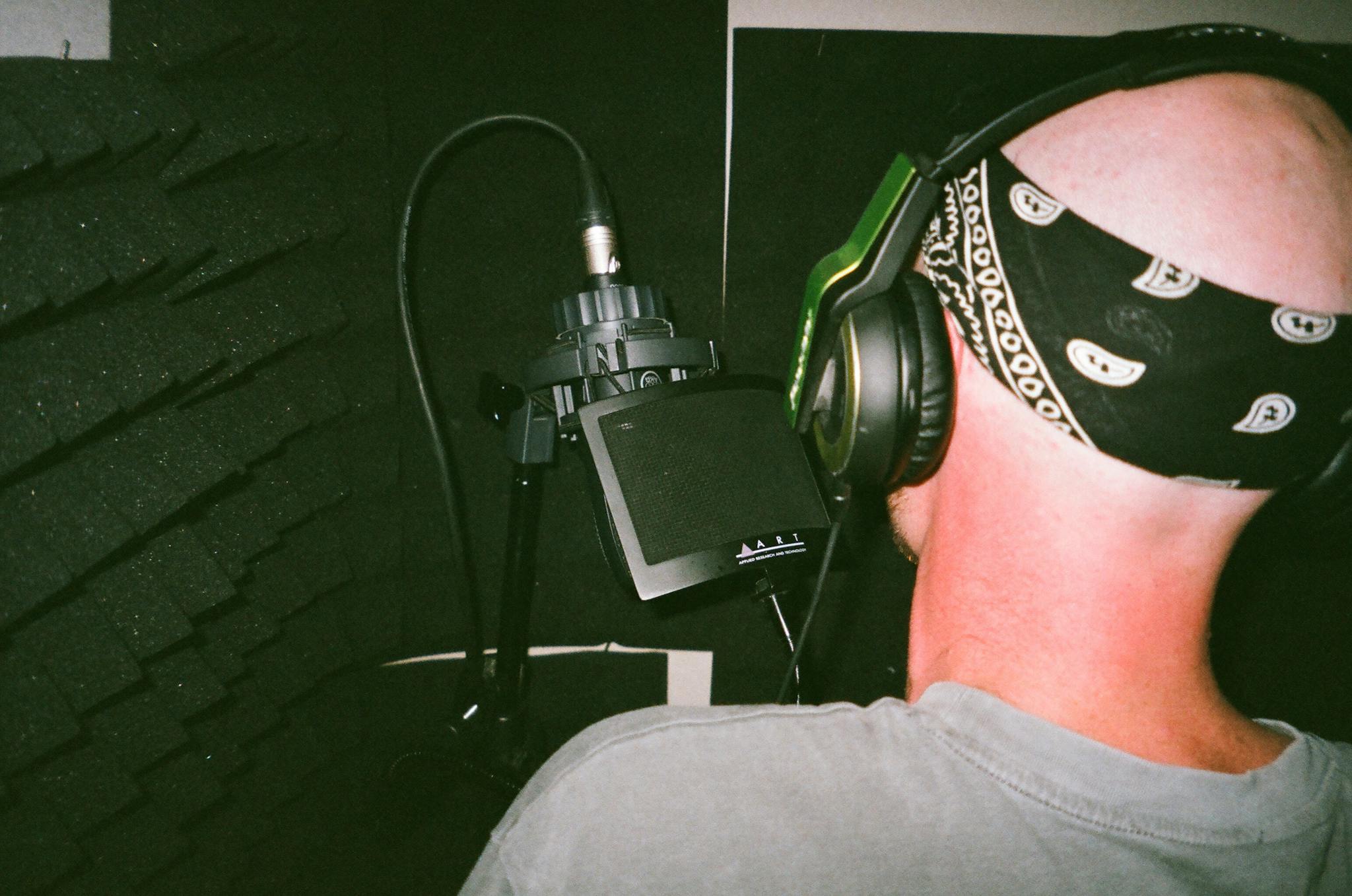 Bald musician recording vocals in studio with headphones and microphone.