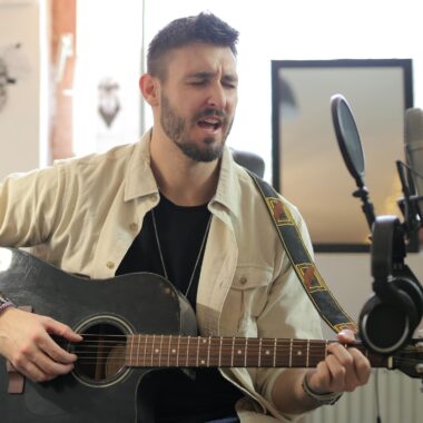 Man singing and playing an acoustic guitar in a professional music studio.