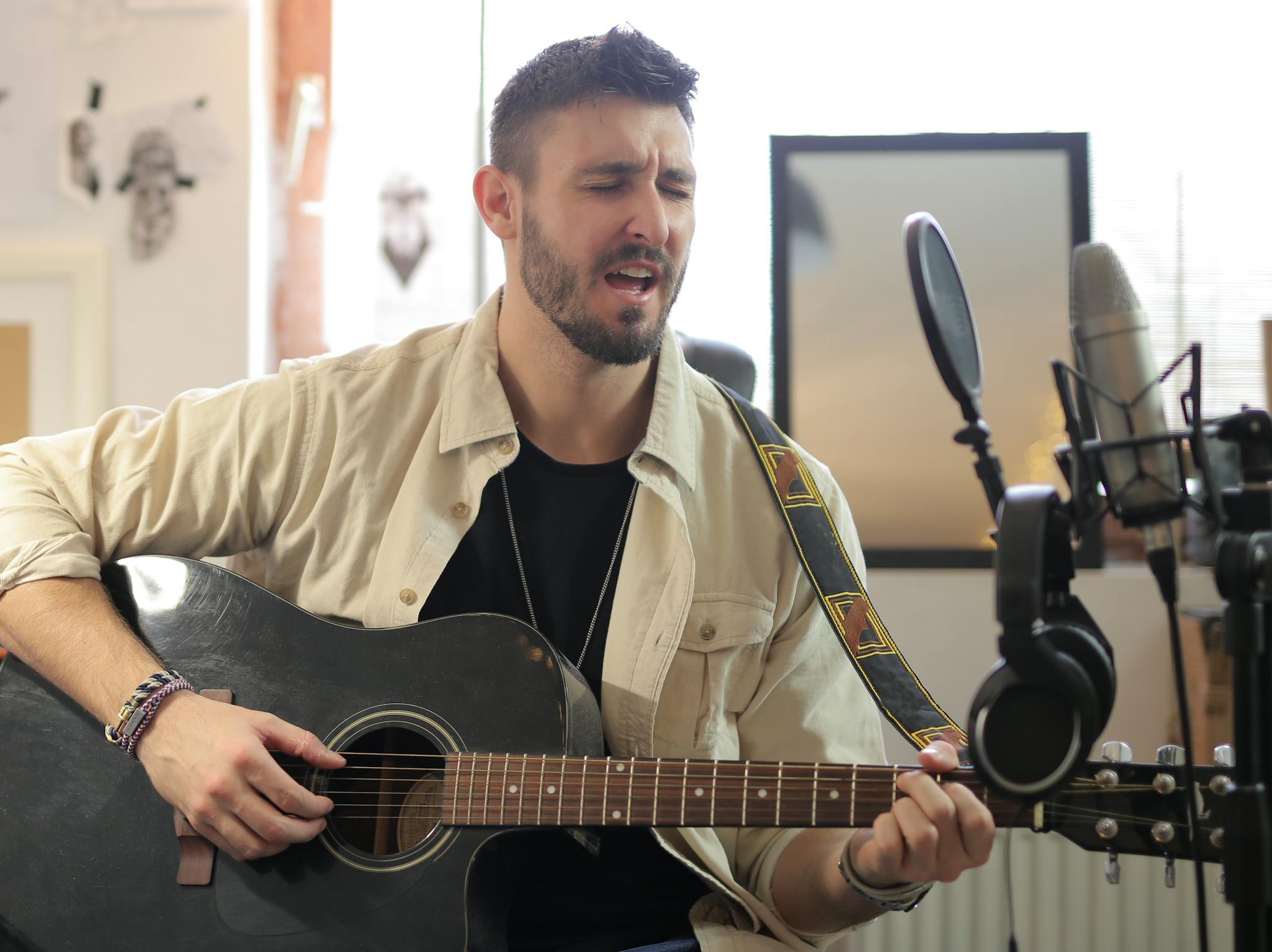 Man singing and playing an acoustic guitar in a professional music studio.
