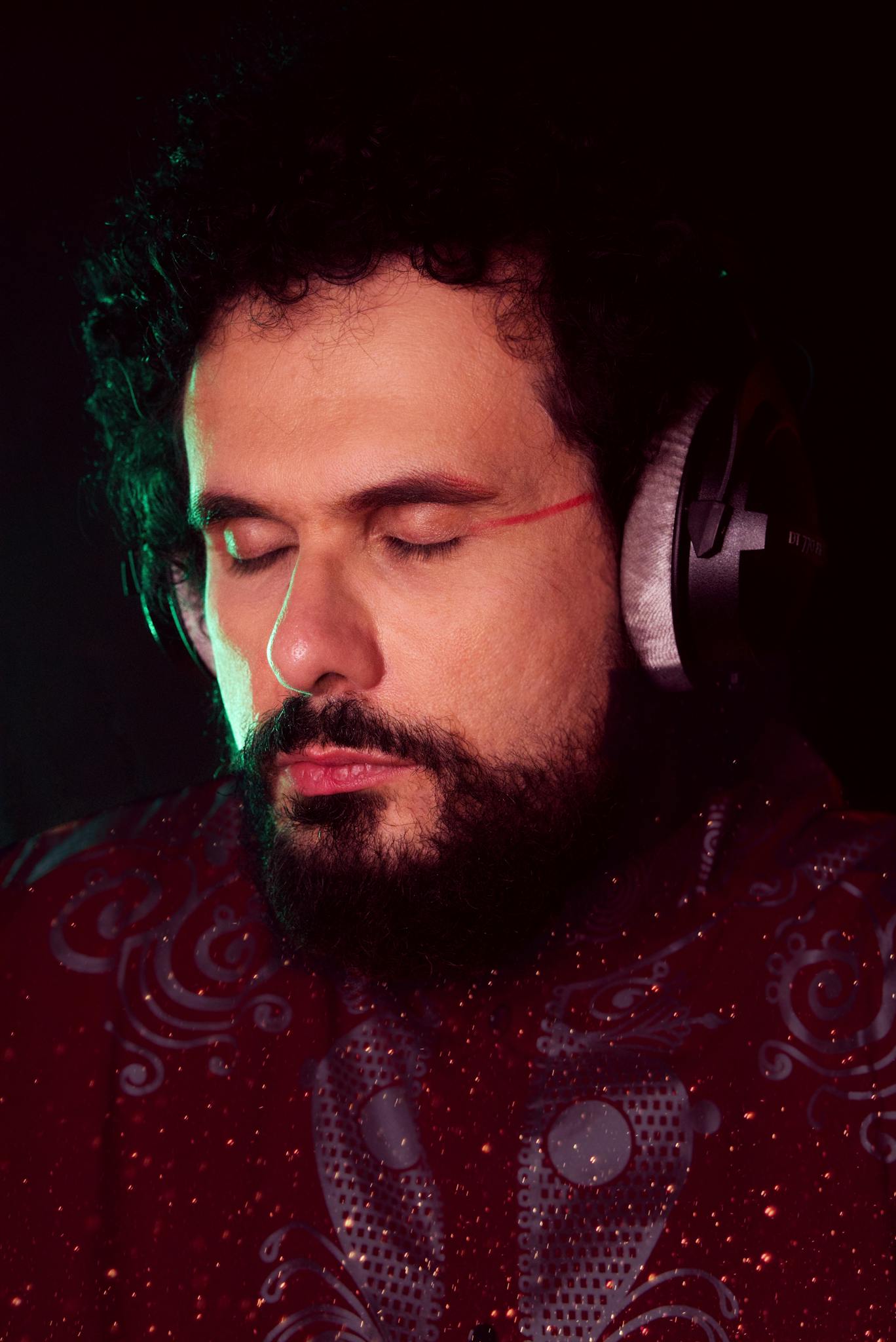 Portrait of a bearded man in a patterned shirt wearing headphones and listening to music.