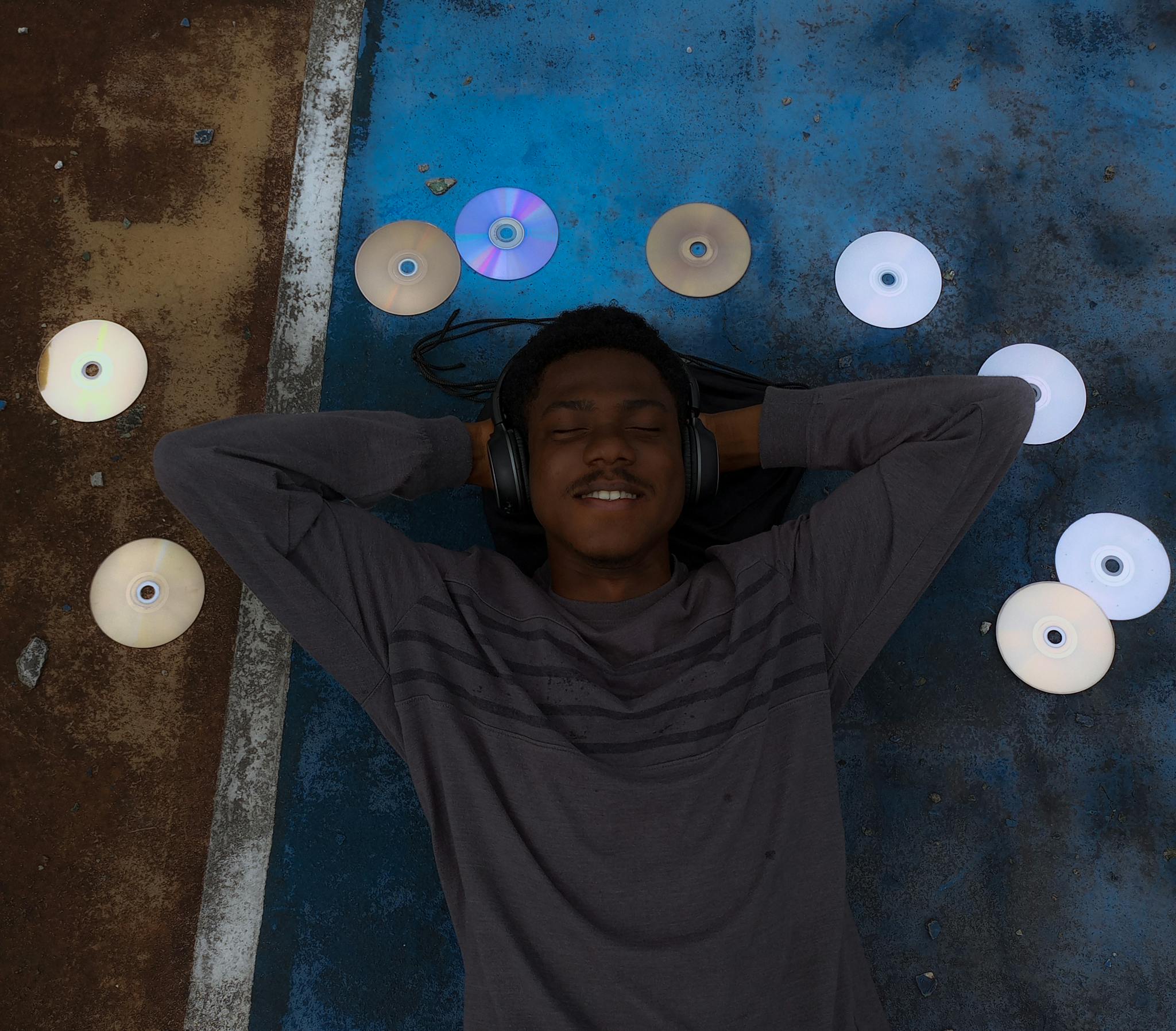 Young man enjoying music with headphones and surrounding CDs, lying on a colorful surface.